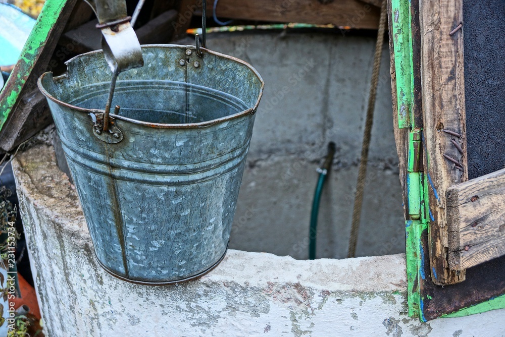 gray metal bucket of water standing on an open well in the street gray metal bucket of water standing on an open well in the street