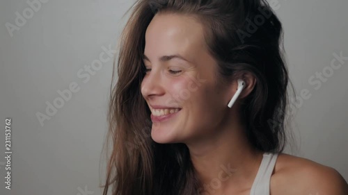 Portrait of a beautiful young, in a leather jacket with airpods in her ear, listens to music. Student dancing happy earpods handsfree bluetooch girl smiling, looking down. photo