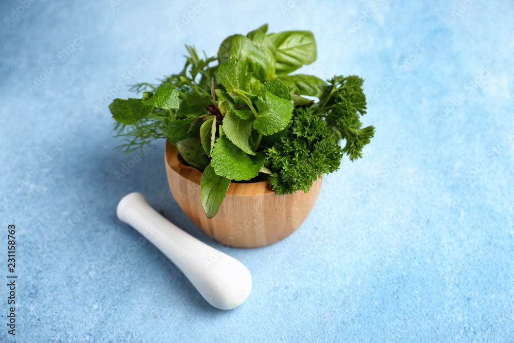 Mortar with fresh aromatic herbs and pestle on color background
