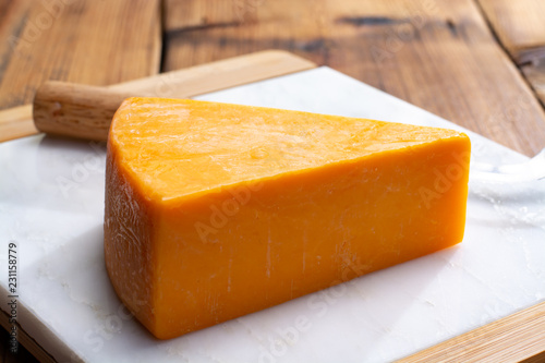 Piece of bright yellow hard cheese cheddar, originating in the English village of Cheddar in Somerset