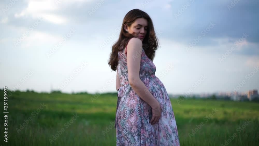 Pregnant girl outdoors stroking her belly and looking at the camera Pregnant girl outdoors stroking her belly and looking at the camera