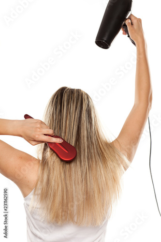 unknown young woman drying her hair with hair dryer on white backgrund