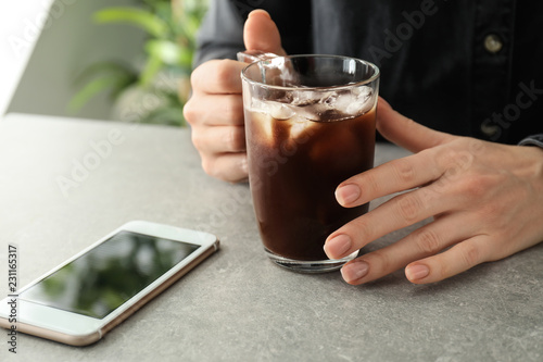 Woman with glass cup of cold coffee and mobile phone at grey table