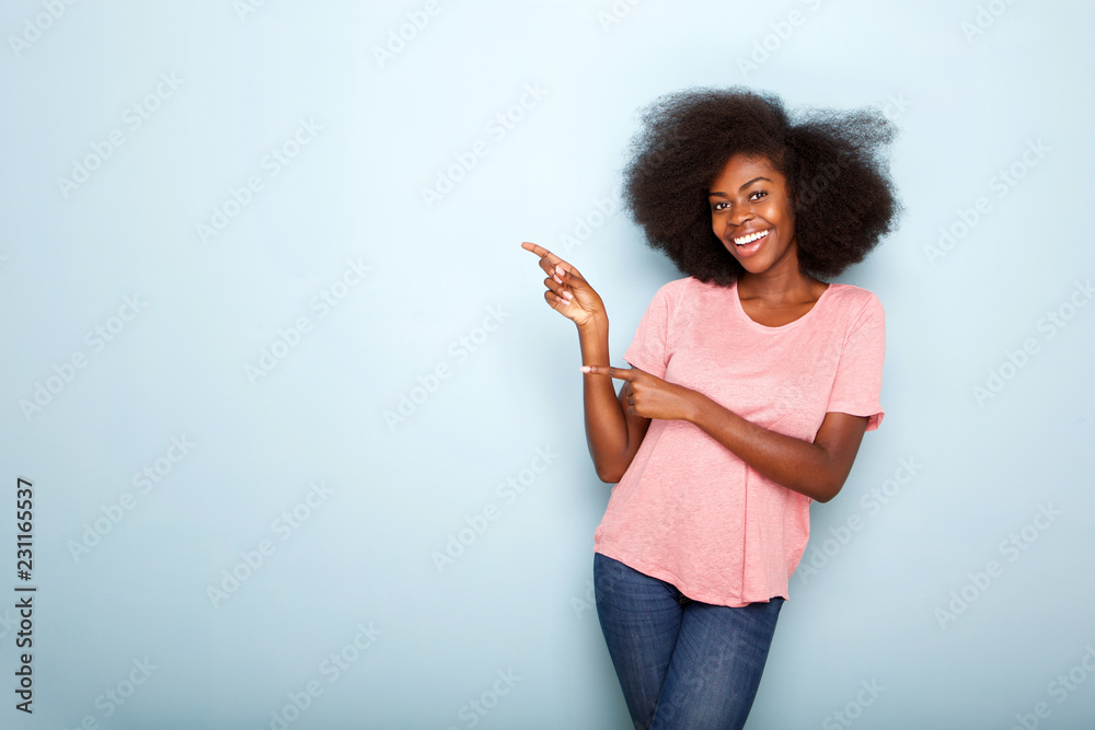 smiling young black woman pointing to copy space on blue background ...