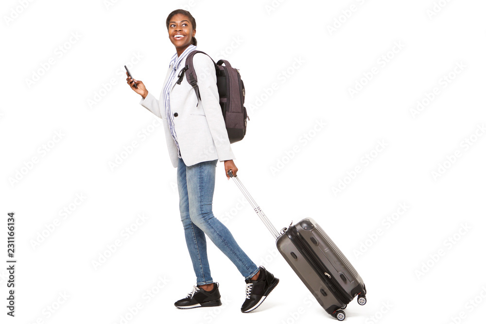 Full length side portrait of happy young black woman walking with luggage and mobile phone Full length side portrait of happy young black woman walking with luggage and mobile phone