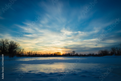 A winter sunset over a small  ice and snow covered lake. Can be used as a sky replacement.