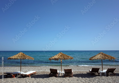 Loungers under palm tree leaves parasols on beach on Samos island, Greece