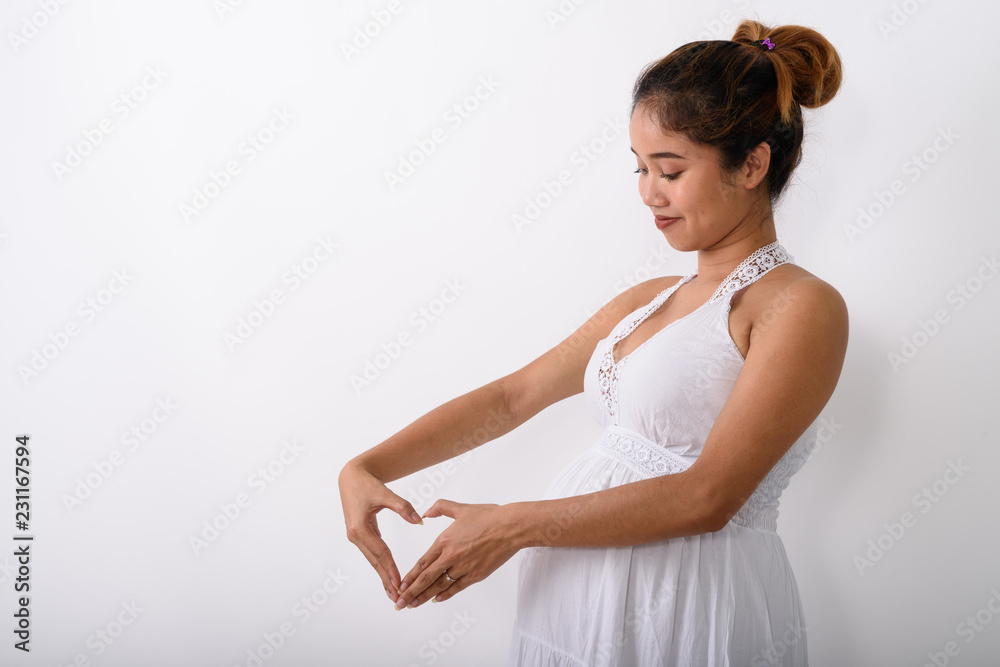 Profile view of young Asian pregnant woman making heart hand sig Profile view of young Asian pregnant woman making heart hand sig