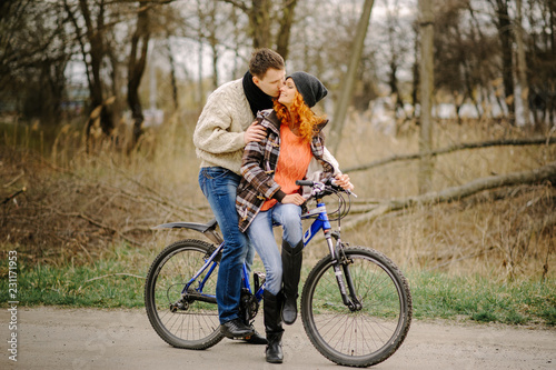 Couple in love is riding the bicycle in the park. Active people. Outdoors. Autumn couple wearing in autumn clothes. Funny couple are getting ready for autumn sale