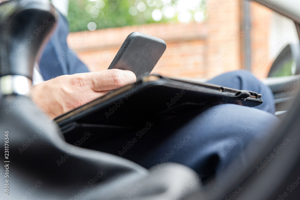 Businessman working on tablet and smartphone inside car on bright day