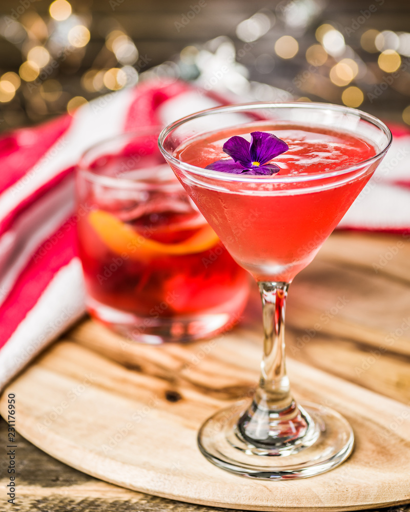 A red colored cocktail with a purple flower, with other cocktails in the background A red colored cocktail with a purple flower, with other cocktails in the background