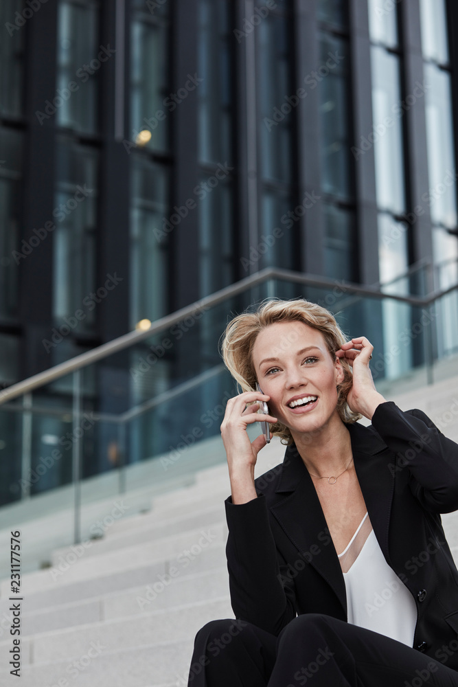 Portrait of smiling young businesswoman on the phone sitting on stairs outdoors Portrait of smiling young businesswoman on the phone sitting on stairs outdoors