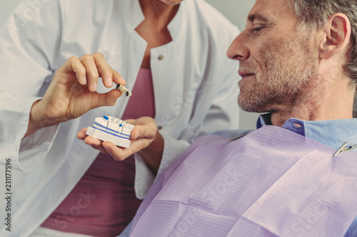 Dentist explaining dental bridge on a tooth model to patient photo