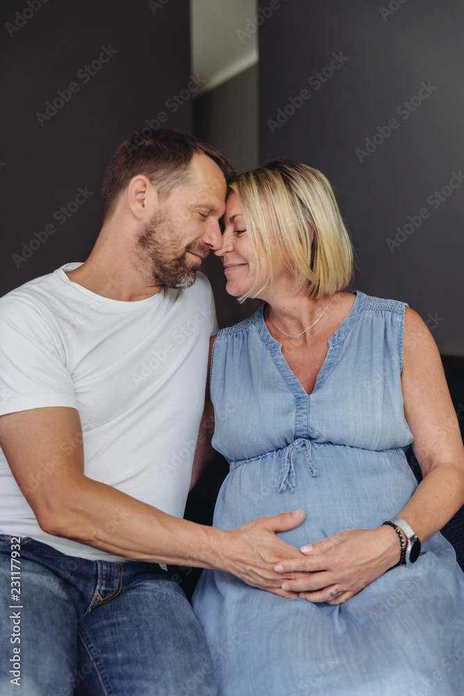 Mature man and his pregnant mature wife sitting on bed touching her