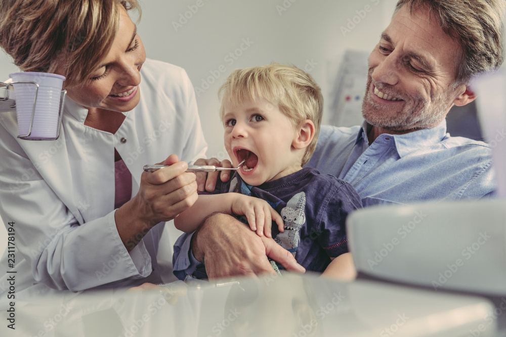 Female dentist examining little boy, sitting on his father's lap Female dentist examining little boy, sitting on his father's lap