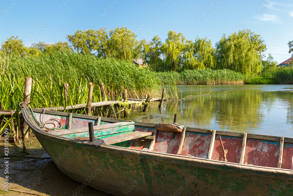 Obraz premium The calm sunny river overgrown with reed and old weathered wooden fishing boat