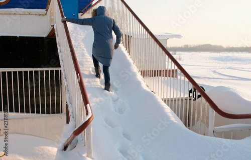 Unrecognizable woman in a blue jacket climbs up a snowy staircase. Back view. photo