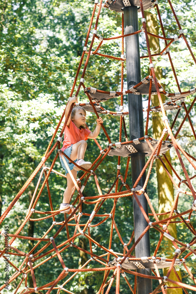Active little child playing on climbing net the playground. A girl play and climb outdoors on sunny summer day. 