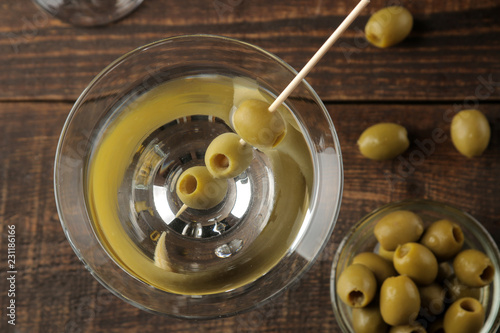 Martini in a glass wineglass with green olives on a skewer on a brown wooden table. cocktails. bar