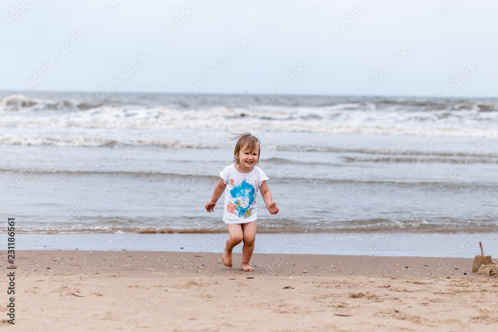 A little girl having fun near the sea, running. A gloomy cloudy day at the sea