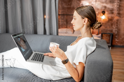 Young woman in white clothes sitting on the couch with laptop at the living room of the modern loft apatment photo