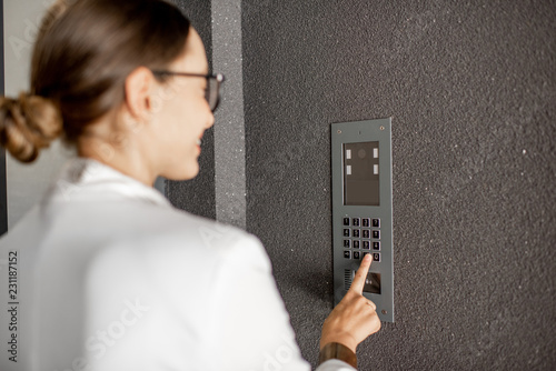 Young business woman in white suit entering code on the intercom keyboard of the residential modern building