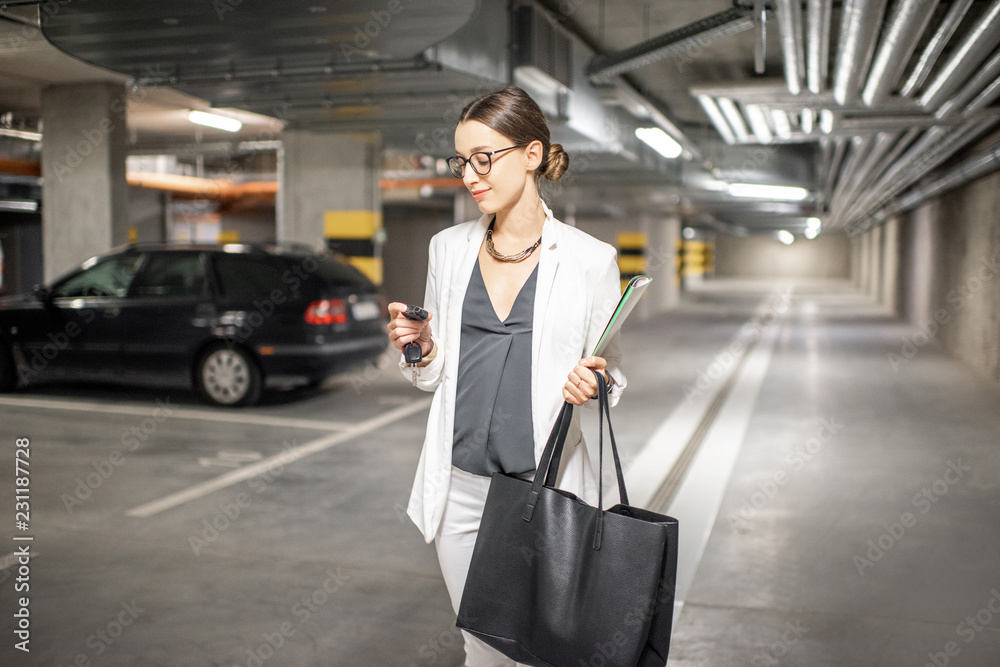 Young business woman walking with car keys in the underground parking of the new residential building Young business woman walking with car keys in the underground parking of the new residential building