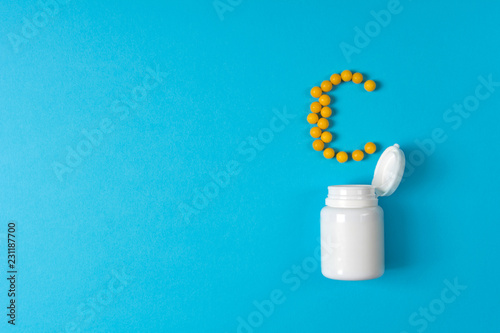 Yellow pills in a vitamin C poured from a medicine bottle on blue background. Medication and prescription pills. Top view. Flat lay. photo