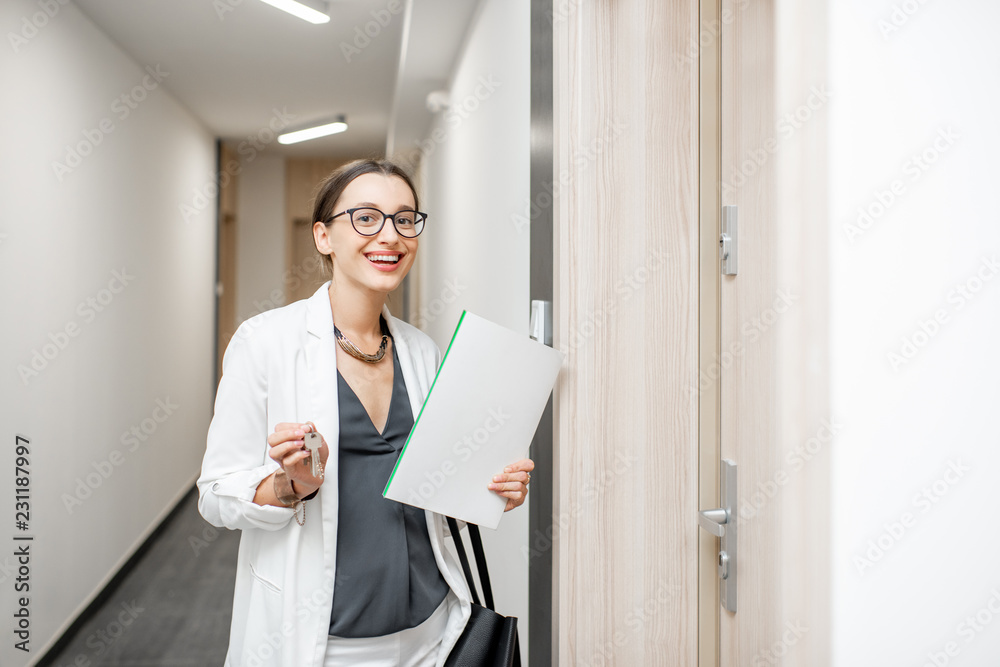 Portrait of an excited woman with key and documents standing near the dooor of the new apartment in the walkhall Portrait of an excited woman with key and documents standing near the dooor of the new apartment in the walkhall