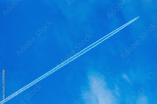 An airplane and a trail from an airplane in a blue sky_