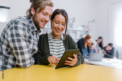 Office lovebirds looking at the tablet in front of their colleagues