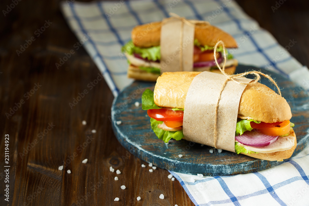 Appetizing sandwich from crispy bread with chicken, tomatoes, lettuce, cheese and spices on a dark wooden background.