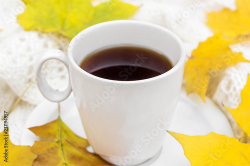 Cup of coffee with white soft scarf and autumn leaves on the table.
