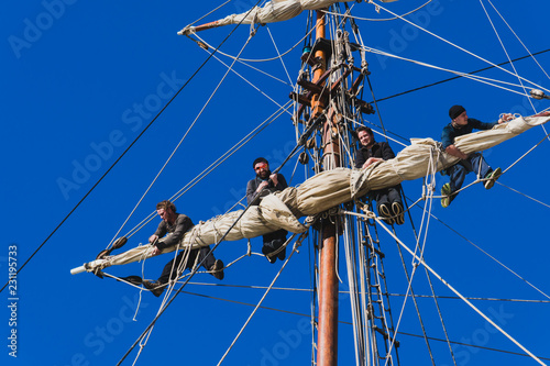Sailors work with sails at a height on a traditional sailboat