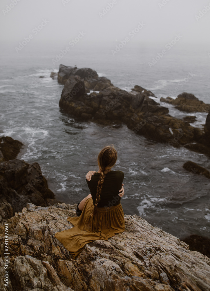 woman with long braid sitting on a foggy rocky coast woman with long braid sitting on a foggy rocky coast