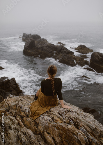 woman with long braid sitting on a foggy rocky coast