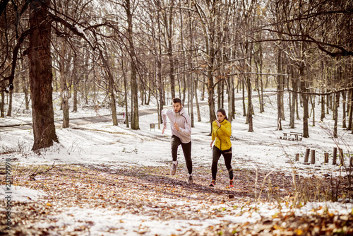 Couple running side by side in woods in winter.