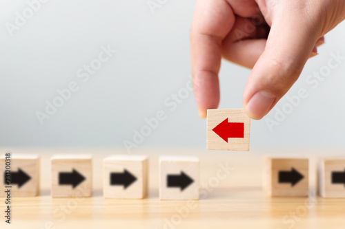 Hand holding wooden block with red arrow facing the opposite direction black arrows, Unique, think different, individual and standing out from the crowd concept