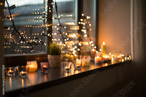 hygge, decoration and christmas concept - candles burning in lanterns on wind...
