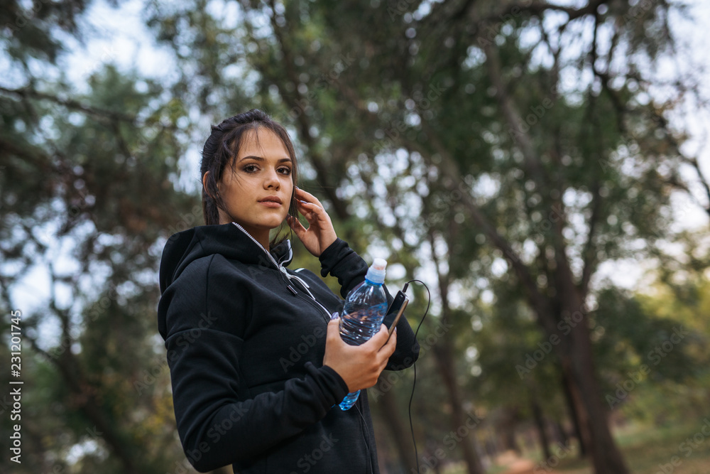 Fototapeta premium Woman jogger holding water and smart phone while exercising in park