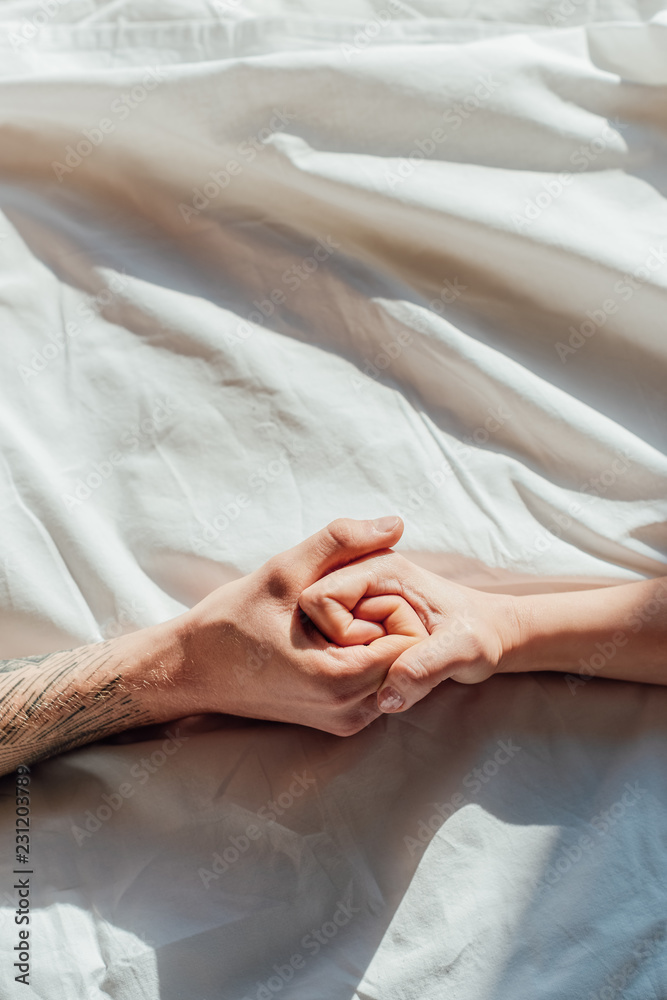 partial view of couple in live holding hads while lying in bed together partial view of couple in live holding hads while lying in bed together
