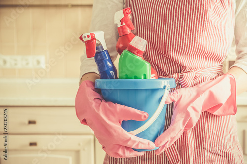 Cleaning concept - female holding cleaning supplies in blue basket, copy space, kitchen background