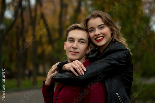girl in a black jacket, smiling, hugging a guy. couple in love in the autumn park. family on vacation, date, lovers. hug from the back, come from the back.