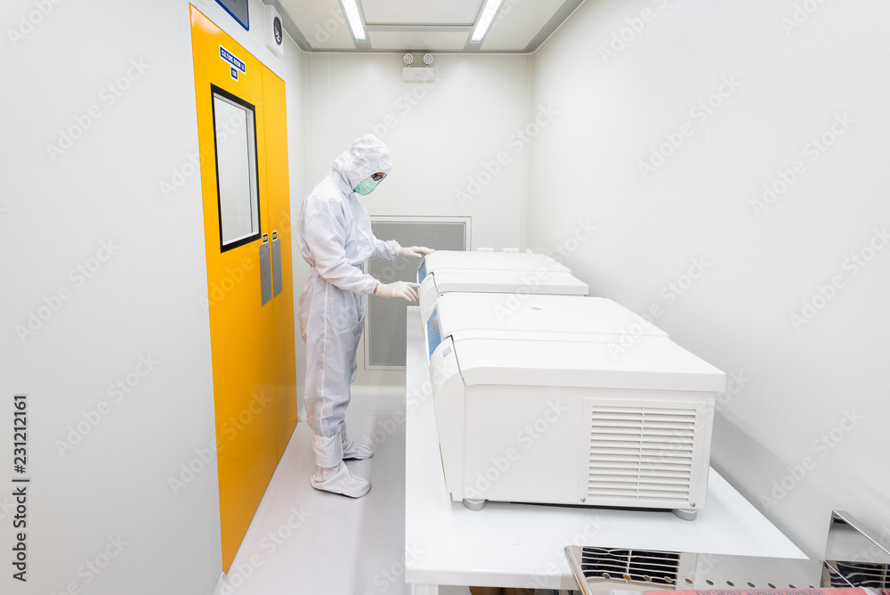 A scientist in sterile coverall gown using laboratory equipment for doing biological research in cleanroom.