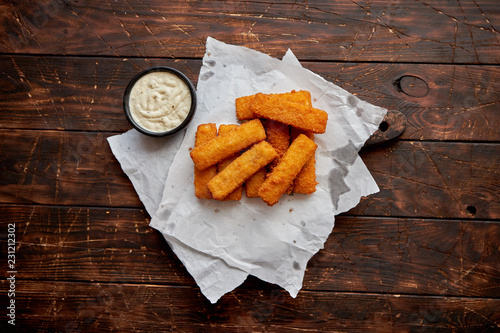 Canvas Print Pile of golden fried fish fingers with white garlic sauce placed on chopping board on dark wooden background