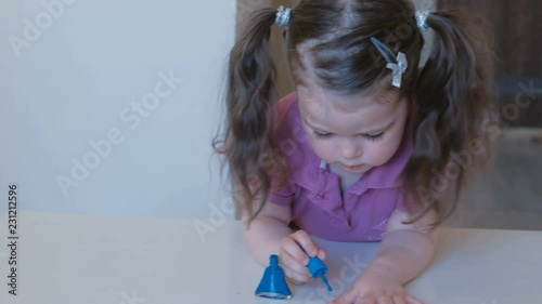 Little cute girl paints her nails with blue varnish. photo