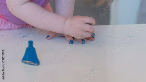 Little cute girl paints her nails with blue varnish. Hands close-up. photo