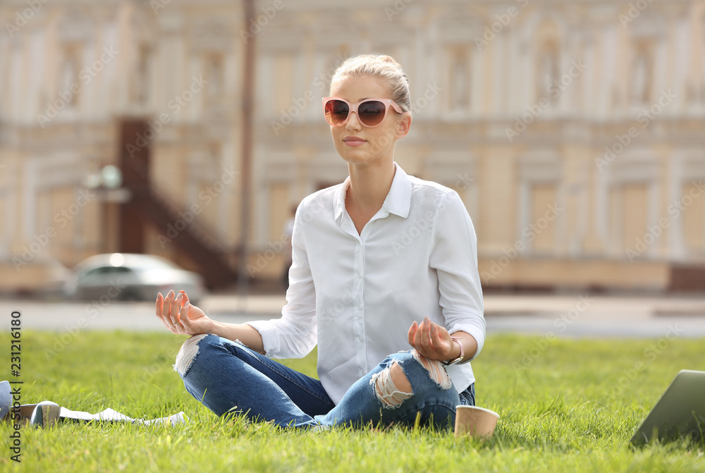 Fototapeta premium Young woman meditating on green lawn in park. Joy in moment