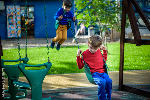 Smiling little boy and his brother friend on a swing. Children playing outdoors in summer. Healthy childhood friendship concept photo