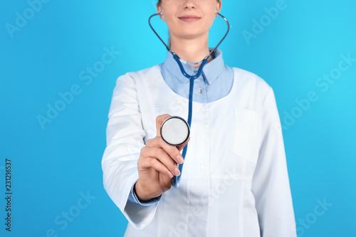 Female doctor holding stethoscope on color background, closeup
